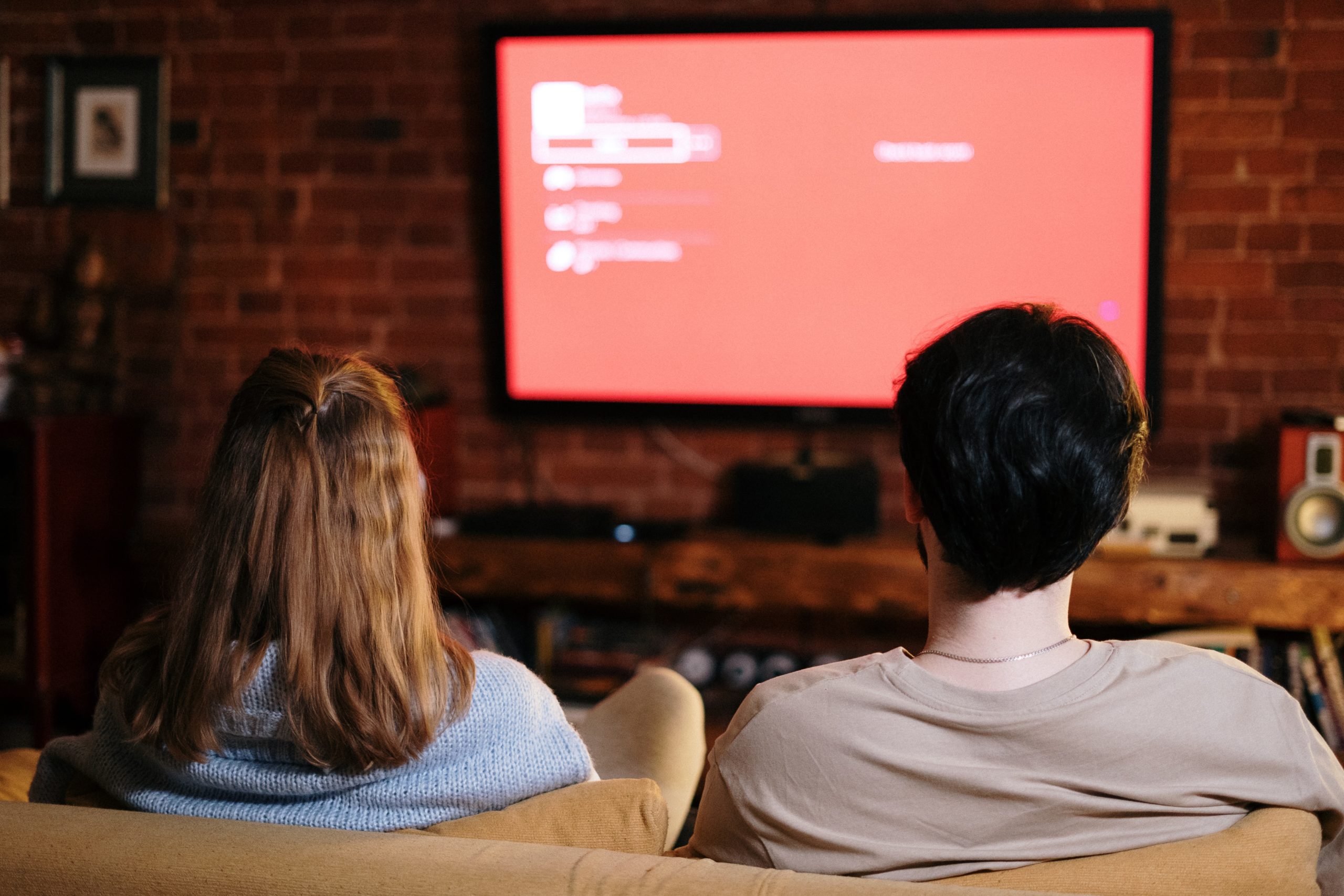 Two teens sitting on a couch watching a movie together