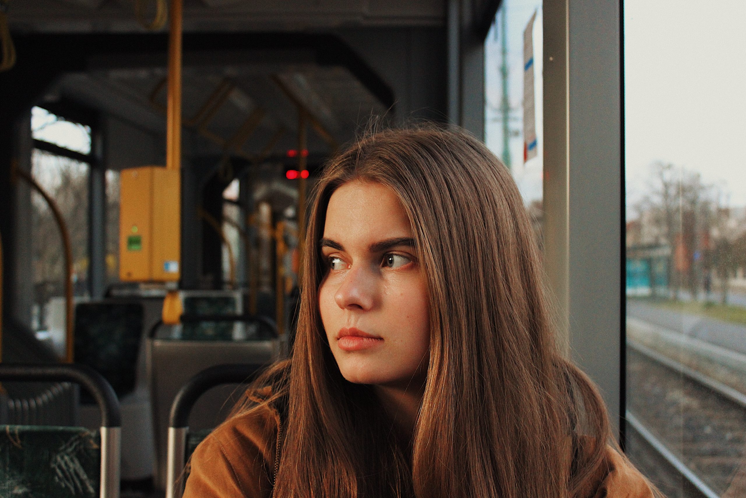 sad looking young woman sitting on a bus looking away from the window