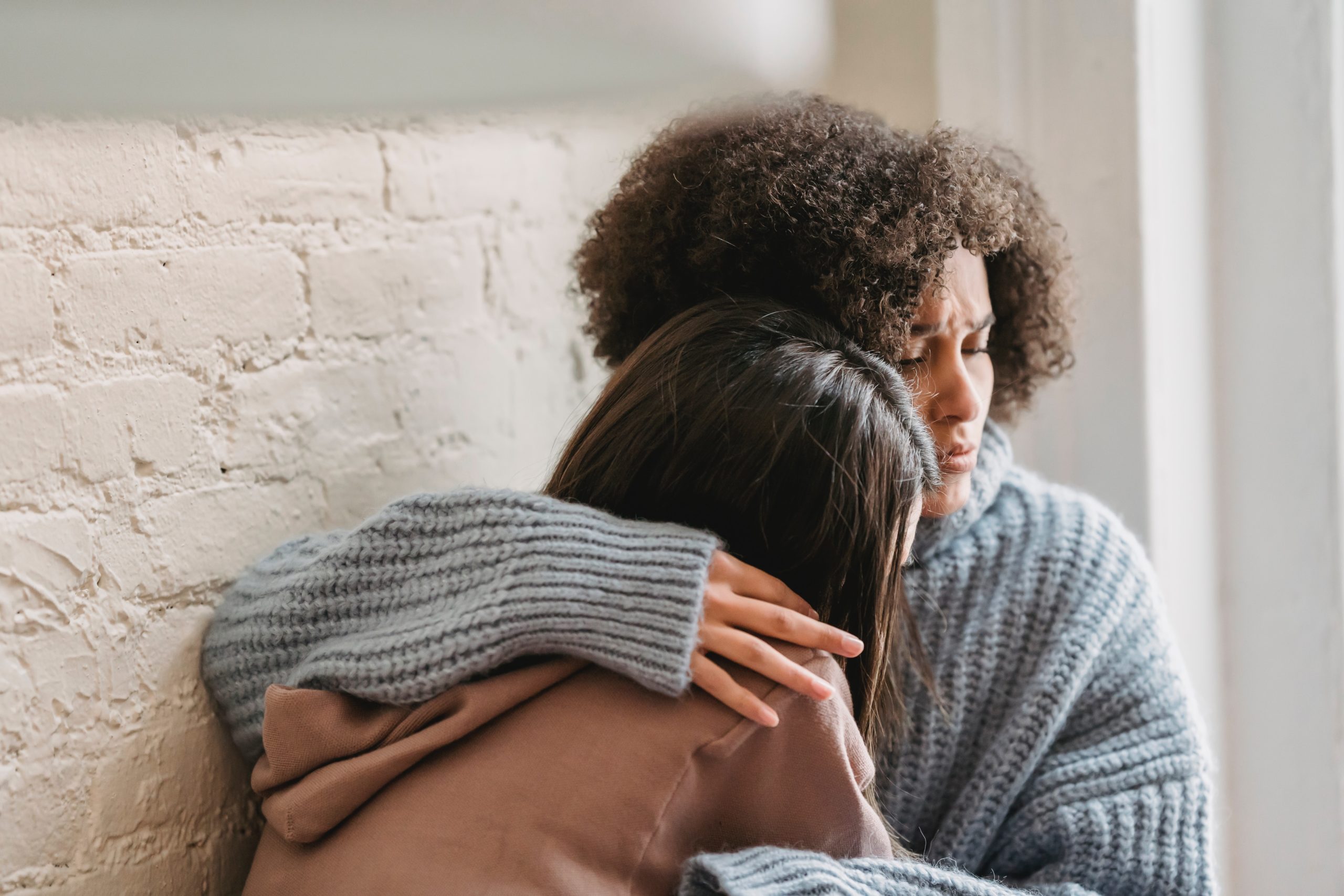 woman comforting another young woman who is upset by wrapping her around her