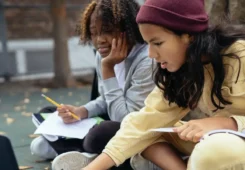 two students doing homework using a computer while sitting outside